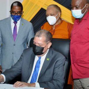 Minister of Industry, Investment and Commerce, Hon. Audley Shaw (seated), signs memorandum of understanding virtually with the International Labour Organisation, on Thursday (February 4), at the offices of the Ministry of Industry, Investment and Commerce in New Kingston. Witnessing the signing are (from left) Minister of State, Ministry of Industry, Investment and Commerce, Norman Dunn; Chief Executive Officer, Jamaica Business Development Corporation, Valerie Veira and Permanent Secretary, Ministry of Industry, Investment and Commerce, Dermon Spence. 